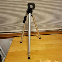 Camera tripod set up on wooden surface showing front view with extended legs and pan-tilt head.