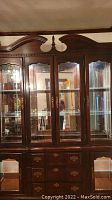 Front view of antique wood china cabinet showing upper glass cabinet with four doors and lower base with drawers and glass doors.