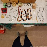 Photo showing multiple bracelets, necklaces, and earrings arranged on a table including green bangle, silver cuff, pearl bracelet, and colorful brooches.