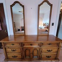 Front view of the dresser with all drawers closed and two arched mirrors mounted above the flat top surface.