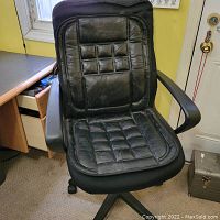 Black executive desk chair showing padded seat and backrest with stitched square pattern. Chair has plastic armrests and a wheeled base.