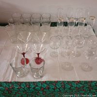 Overview of assorted glassware placed on white cloth with holly patterned border, includes coffee mugs, tall glasses, wine glasses, martini glasses, and champagne flutes.