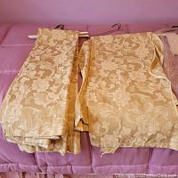 Folded gold floral pattern curtain panels with rod pockets, laid on a pink surface.
