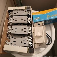 Multiple gray Leviton electrical outlets stacked in box with a white Decora dimmer switch visible on the side with black wiring attached.