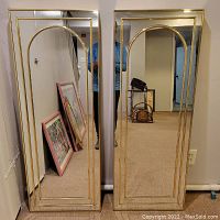 Two tall matching rectangular mirrors with gold trim and an arch detail on top inside border, standing side by side.