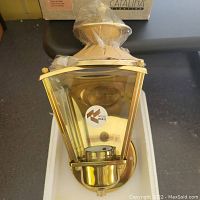 Close-up of the face of the solid brass outdoor light showing clear glass sides, brass detailing, and a sticker indicating solid brass material.