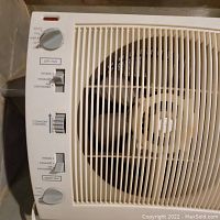 Close-up photo showing a white Holmes portable window fan's control panel including speed dial, intake/exhaust slider, and comfort control slider.