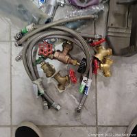 Flexible braided hoses with brass valves and red-handled manual shutoff valves on tiled floor