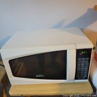 White Sunbeam microwave with digital keypad and door closed, showing Sunbeam logo on door window and display time on keypad screen.