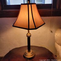 Front view of bronze metal table lamp with beige fabric shade illuminated.