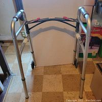 Front view of the lightweight aluminum walker showing padded hand grips, height adjustable legs with locking pins, and dual front wheels.