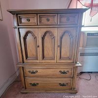 Front view of the wood armoire showing three small drawers on top, a cabinet with two doors in the middle, and two large drawers at the bottom.