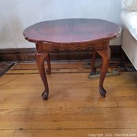Wood end table shown front side displaying curved legs and scalloped edge tabletop.
