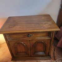 Front view of wood night stand showing top surface with water stain marks, drawer with brass knob, and double cabinet doors with carved panels.