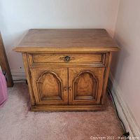 Front view of the wood night stand showing its drawer and cabinet doors closed. Visible wood grain and metal handle on drawer.