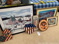 Seven Americana art and decor items arranged on the floor including two large framed reproduction paintings, a rooster clock, two American flag heart decorations, an Americana stars and stripes sign, and a small framed rooster print.