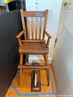 Antique wooden high chair shown front facing with armrests and slatted backrest.