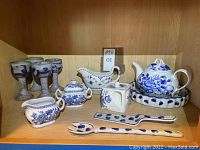 Blue and white porcelain serving set including teapot, sugar bowl, creamer, square container, serving utensils, and four blue pottery wine glasses.