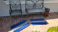 Overview showing metal loveseat and chair with cushions, bamboo umbrella stand and two door mats on brick floor