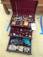Top view of open wooden jewelry box showing lid compartment with hanging necklaces and top drawer with assorted rings and earrings