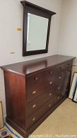 Full side and front view of dark wood dresser with nine drawers and matching wooden framed wall mirror above it.