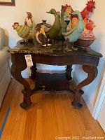 Full view of the Victorian style table with black and caramel marble top, dark wooden curved legs, lower shelf, and several decorative wooden birds on top for scale.