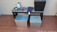 Wooden garden bench, two silver metal storage boxes, three black metal storage boxes stacked inside each other, and kneeling pad visible on top of bench