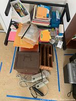 Top-down view of assorted paper pads, envelopes, file boxes, power strips, and wicker organizer on and around a small table frame.