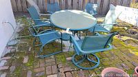 View of patio table with six mesh chairs arranged around it on brick and stone patio.