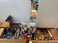 Wide view of kitchen drawers with stainless steel cutlery trays and utensils in red crock, plus knife block on counter.