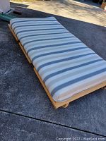 Futon fully laid out showing striped cushion on pine wood frame