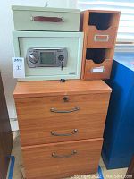 Photo showing American Security DL 000 small safe, wooden cabinet with drawers, two-drawer desktop organizer, and lock box on top