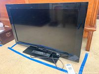 Sony Bravia 32 inch flat screen TV with attached stand and remote lying on carpeted floor near wooden furniture.