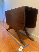 Side angle of wooden drop leaf table with one leaf down showing ridged legs and brass foot caps.