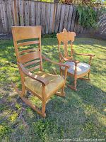 Two wood rocking chairs pictured outdoors on grass, one with slat back and yellow upholstery, other with carved back and patterned upholstery.