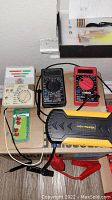 Photo showing three multimeters and a battery jump starter with clamp leads on a tabletop.