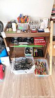 Photo of wooden bookcase filled with various hand tools in plastic containers, electrical parts, and accessories on and inside shelves.