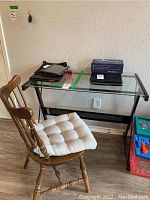 Side view of glass top desk with metal frame and wooden chair with cushion