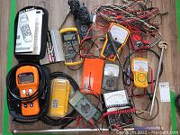 Photo showing various diagnostic devices including multimeters, an orange Autoscanner, and numerous cords.