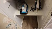 Shelf containing Black & Decker steam iron, small travel iron with gray carry case, and ironing board below.