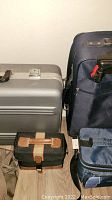 Photo showing a silver hard-shell suitcase, a large blue soft luggage bag, and a small black and brown travel bag on the floor.