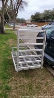 Metal wheelchair lift carrier with ramp folded upright beside vehicle, showing mesh ramp and platform.