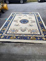 Full view of cream/beige rectangular area rug with floral pattern and bold blue decorative border.