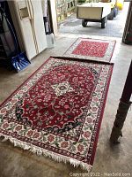 Two floral pattern area rugs laid on garage concrete floor, one larger and one smaller, both with fringed edges and complex floral designs.