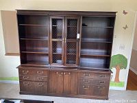 Front view of the wooden bookcase showing shelves, drawers, and cabinets with mesh doors.