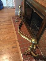 Full view of brass andiron and part of fireplace skirt showing the round finial and curvature