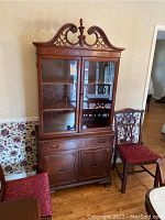 Full front view of the wooden china cabinet with glass doors, drawer, and lower cabinets, accompanied by a chair.