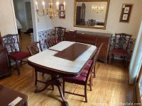 Photo of dining room chairs around a table showing the artful carved wood backs, red upholstered seats, and wood finish.