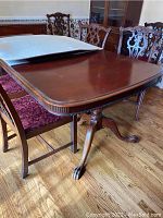 Complete view of wooden dining table with removable leaf and table pads placed on top, surrounded by matching upholstered chairs.