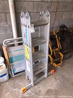 Folded Krause aluminum folding ladder with orange foot caps, stored upright showing side profile and rungs.